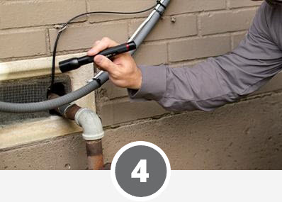 A man using a hose to inspect a pipe for home pest control purposes.