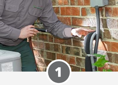 A man is working on an air conditioner in front of a brick wall at home.