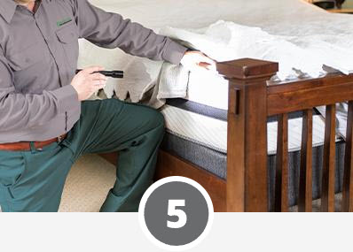 A man is ensuring pest control by putting a mattress protector on a bed.