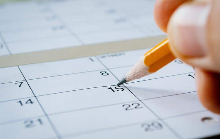 A person is writing on a calendar with a pencil, ensuring their Ornamental Care In Tarrant County,Inc. tasks are organized and scheduled properly for Trees Hurt Too.