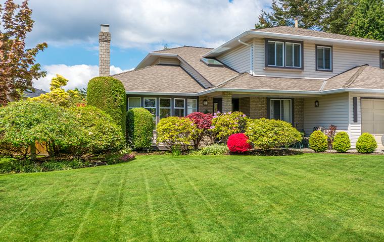 A home with a large lawn and bushes in the front yard, offering a Total Package Service for landscaping needs.