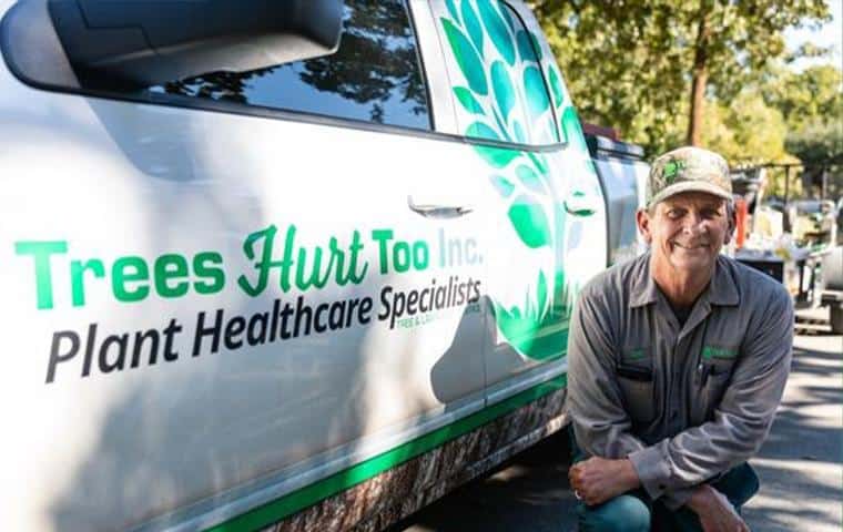 A man kneeling in front of a truck with the words Trees Hurt Too, promoting Tree Care In Tarrant County, Inc.